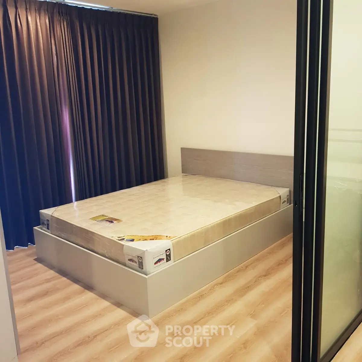 Modern bedroom with new mattress and wooden flooring, featuring floor-to-ceiling curtains for privacy.