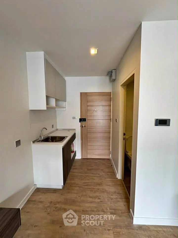 Modern compact kitchen with wooden flooring and sleek cabinetry in a cozy apartment.