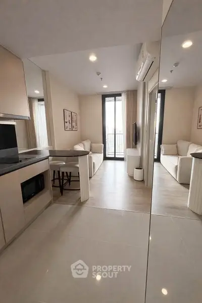 Modern living room with open kitchen, featuring sleek design and natural light from large windows.
