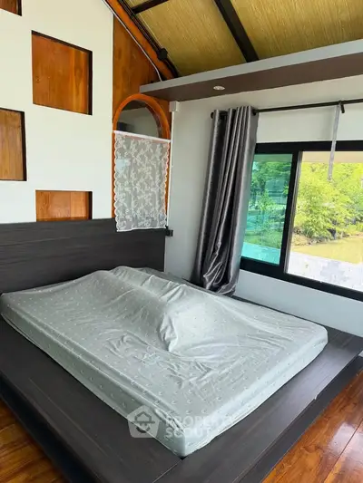 Modern bedroom with large window and stylish wooden accents, offering a serene view of lush greenery.
