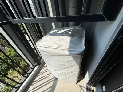 Compact balcony with protective cover on outdoor unit, offering urban views and modern railing design.