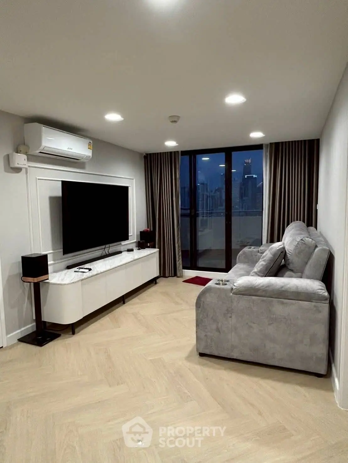Modern living room with city view, featuring sleek furniture and large TV setup.