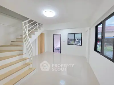 Spacious modern living room with staircase and large windows in a bright, minimalist home.
