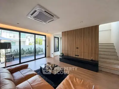 Spacious modern living room with leather sofa and large glass doors to patio.