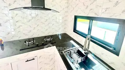 Modern kitchen with sleek black countertop and gas stove, featuring stylish marble backsplash and large window.