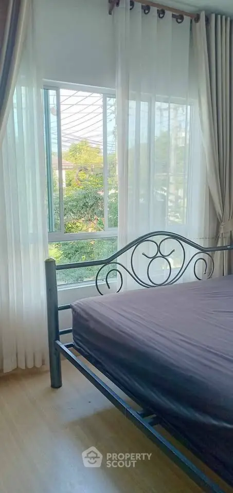 Bright bedroom with large window and elegant metal bed frame, offering a serene garden view.
