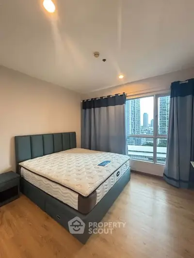 Spacious bedroom with large window offering stunning city views in modern apartment.