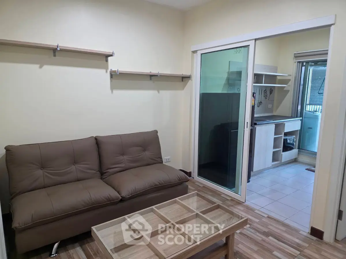 Cozy living room with brown sofa and glass coffee table, adjacent to compact kitchen.