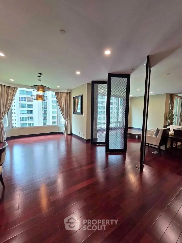 Spacious modern living room with hardwood floors and large windows offering city views.