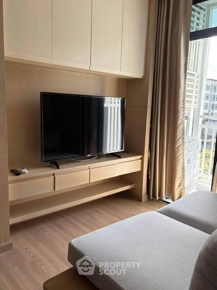 Modern living room with sleek TV setup and large window view in stylish apartment.