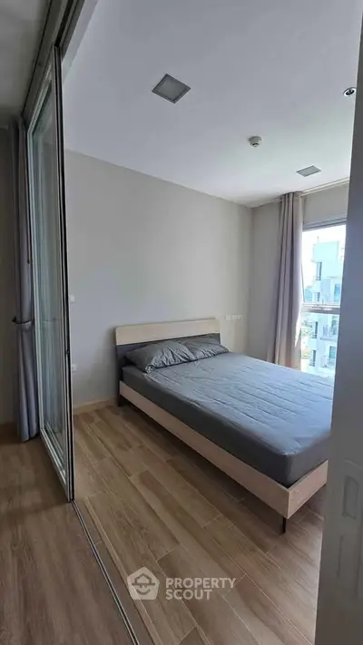 Modern bedroom with wooden flooring and large window in a stylish apartment.