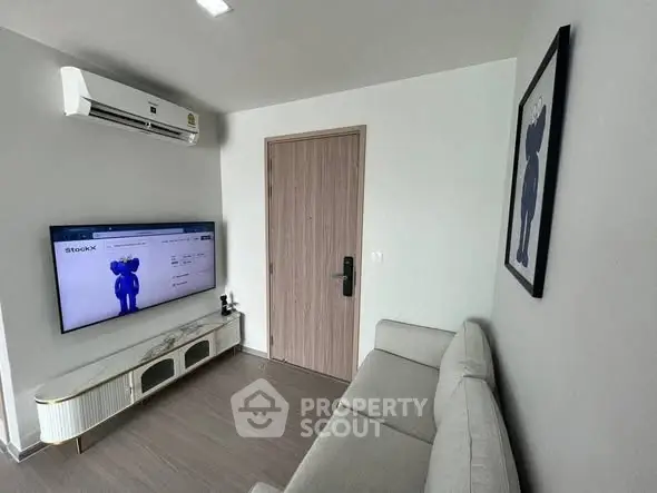 Modern living room with sleek furniture and wall-mounted TV, featuring minimalist decor and air conditioning.