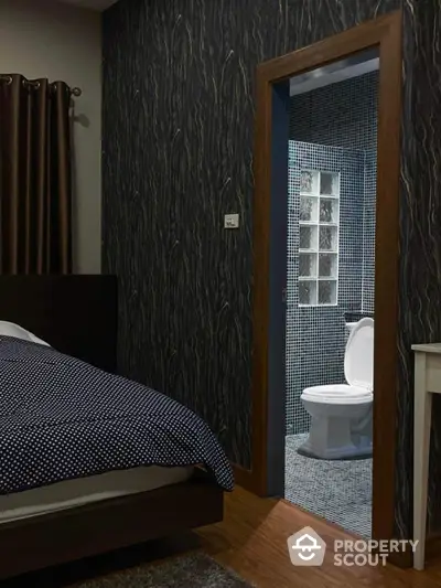 Cozy bedroom with stylish dark wallpaper and en-suite bathroom, featuring a comfortable bed and elegant wooden finishes.