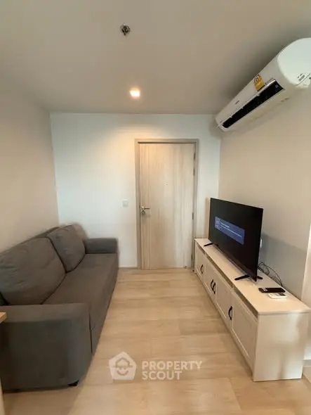 Modern living room with sleek sofa and wall-mounted TV, featuring minimalist design and air conditioning.