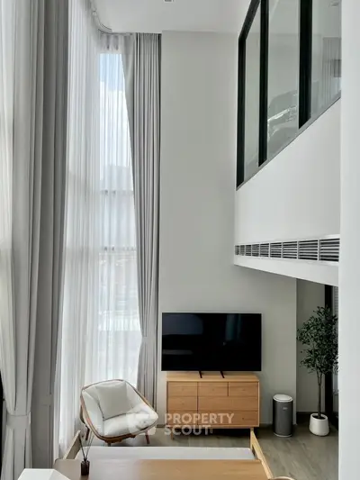 Modern living room with high ceilings and large windows, featuring stylish furniture and a TV.