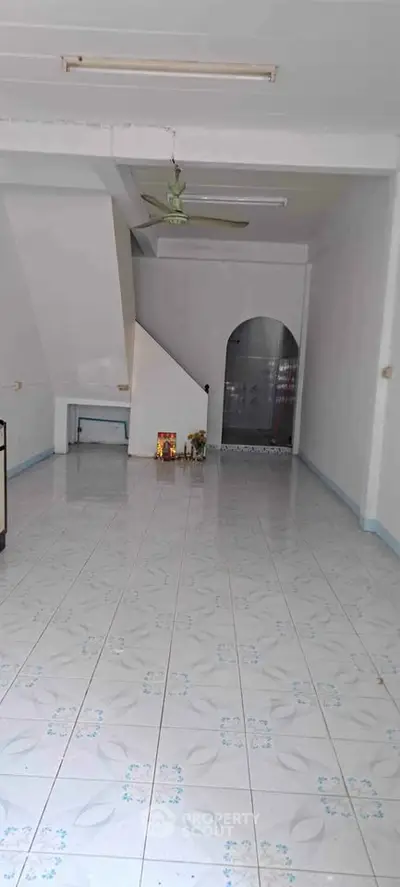 Spacious tiled room with ceiling fan and archway, ideal for versatile use.