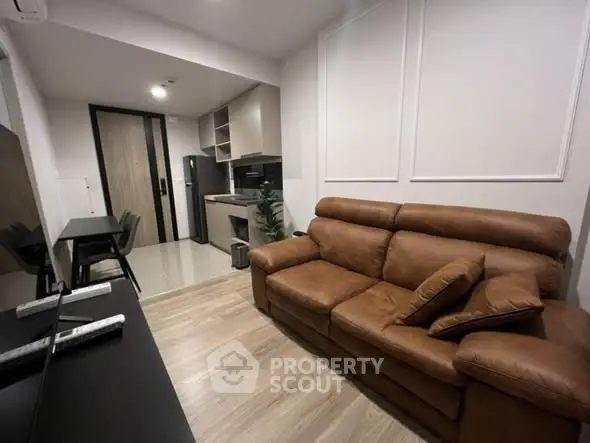 Modern living room with brown leather sofa and sleek kitchen area.