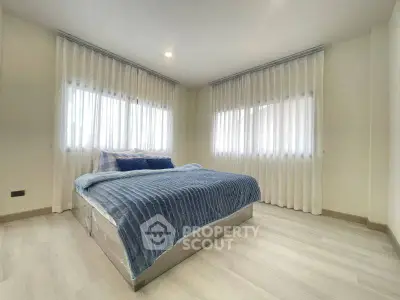 Spacious bedroom with large windows and elegant curtains, featuring a cozy bed and modern decor.