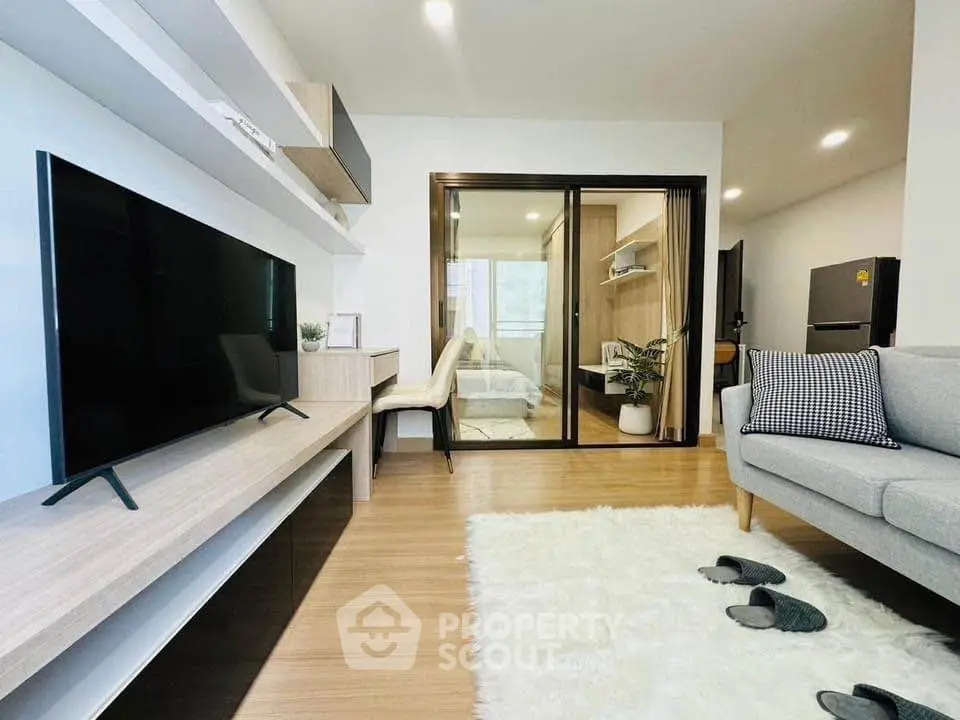Modern living room with sleek TV, cozy sofa, and stylish decor leading to a bright bedroom.