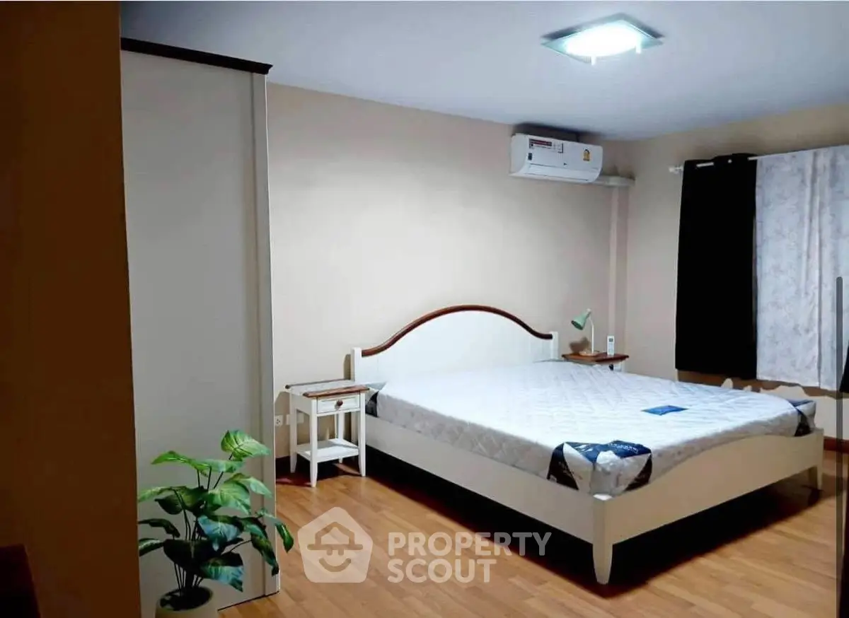 Spacious bedroom with modern decor and wooden flooring, featuring a comfortable bed and air conditioning.