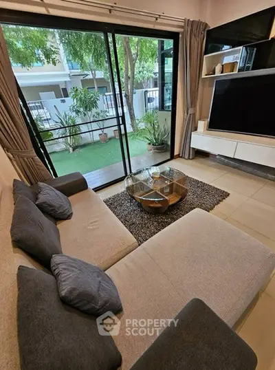 Modern living room with large sofa, glass coffee table, and sliding doors to garden view.