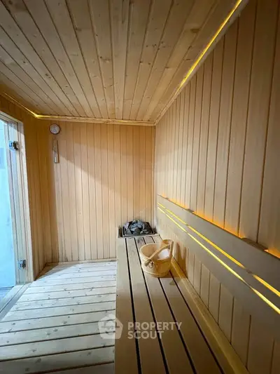 Luxurious wooden sauna with warm lighting and traditional bucket, perfect for relaxation.
