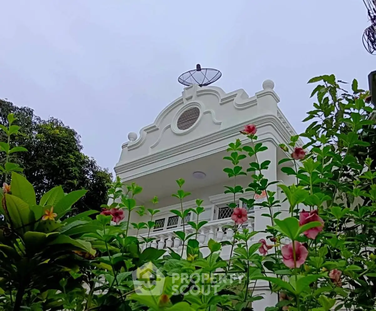 Charming white building with ornate balcony and lush garden view