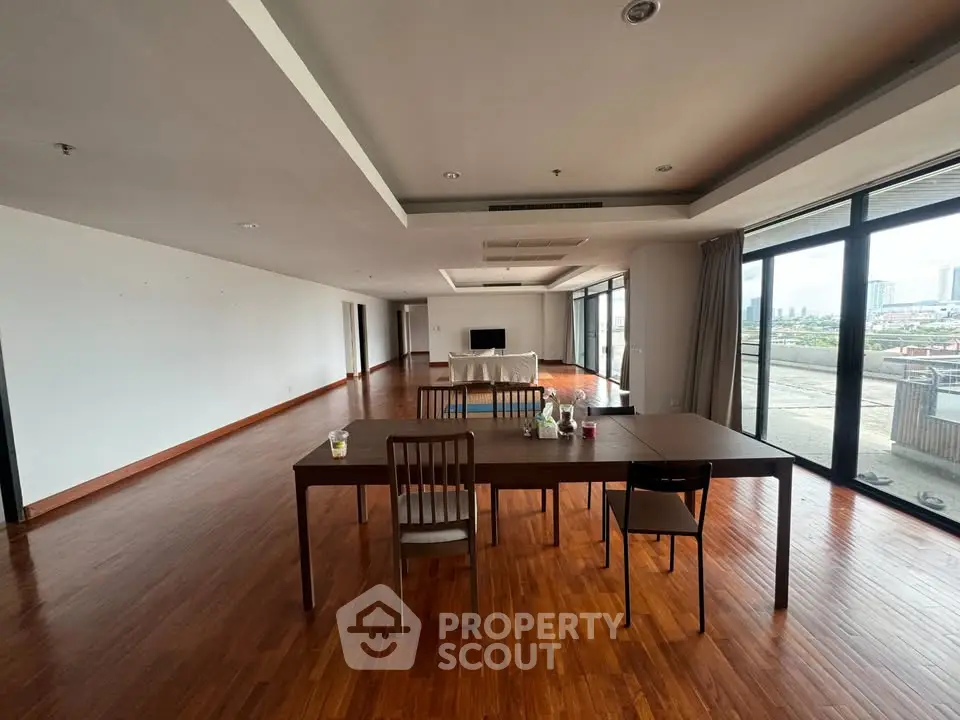 Spacious modern living room with wooden flooring and large windows offering city views.