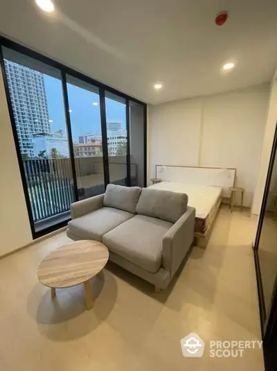 Modern minimalist living room with large windows offering ample natural light, featuring a comfortable grey sofa and a chic wooden coffee table, perfect for urban living.