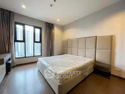 Spacious bedroom with large window and modern decor in a high-rise apartment.