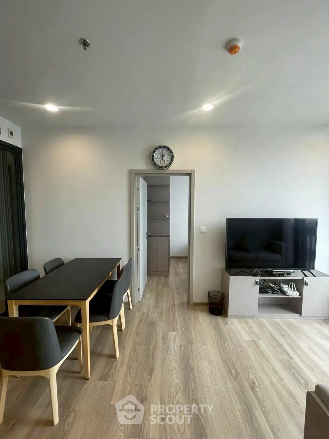 Modern living room with dining area and flat-screen TV, featuring sleek wooden flooring.