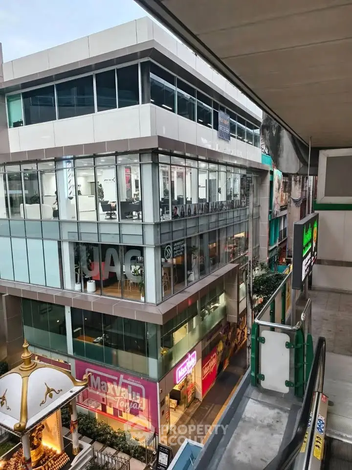 Modern commercial building exterior with glass facade and retail shops in urban setting.