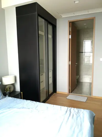 Modern bedroom with sleek wardrobe and en-suite bathroom, featuring elegant design and natural lighting.