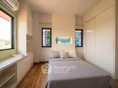 Cozy bedroom with wooden flooring, large windows, and built-in storage in a modern home.