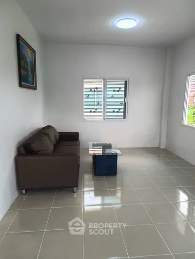 Spacious living room with modern sofa and glass coffee table, featuring natural light from large windows.