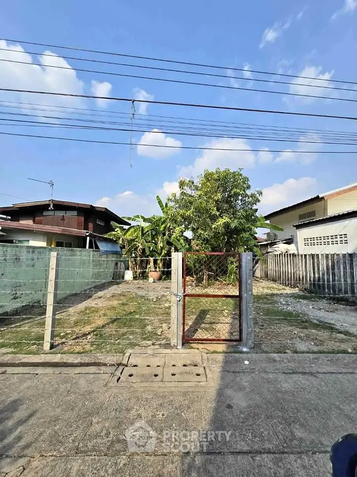 Vacant land plot with potential for development in a residential area, featuring clear blue skies and surrounding homes.