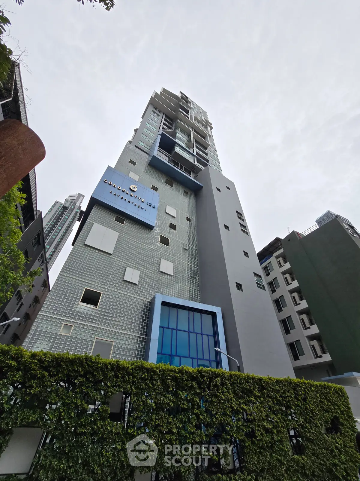 Modern high-rise building with sleek architecture and lush greenery at the base, showcasing urban living.