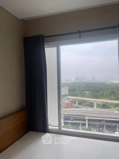 Cozy bedroom with large window offering stunning city and greenery views, perfect for urban living.