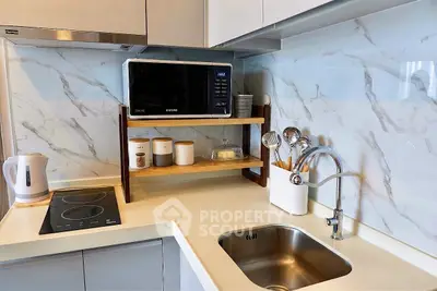 Modern kitchen with sleek appliances and marble backsplash, featuring a microwave and induction cooktop.
