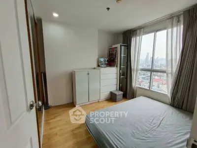 Bright bedroom with large window offering city views, featuring wooden flooring and modern furniture.