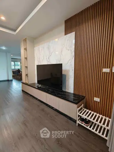 Modern living room with sleek TV unit and marble accent wall, featuring elegant wood paneling and open layout.