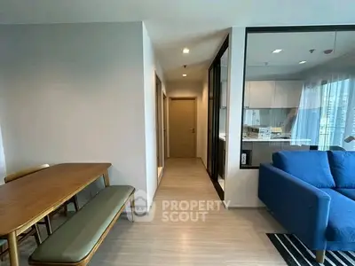 Modern open-plan living room with dining area and kitchen, featuring sleek furniture and large windows.