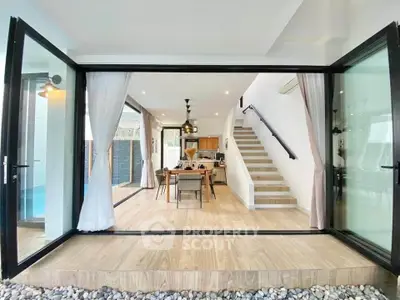 Spacious open-plan living area with modern kitchen and dining, featuring large glass doors and elegant staircase.