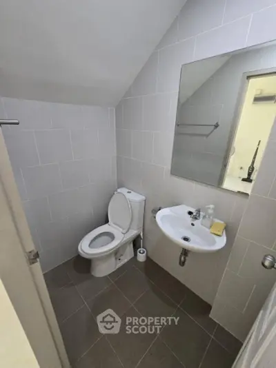 Compact modern bathroom with pristine white tiles, pedestal sink, and well-maintained toilet, ideal for urban living spaces.