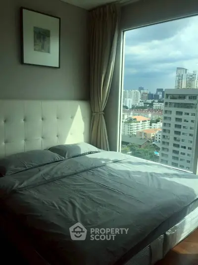 Modern bedroom with large window offering stunning city view in high-rise apartment.
