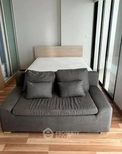 Modern studio apartment with cozy sofa and bed, featuring sleek wood flooring and large windows.