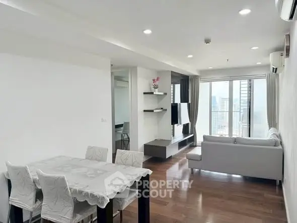 Spacious modern living room with dining area and city view, featuring elegant decor and natural light.