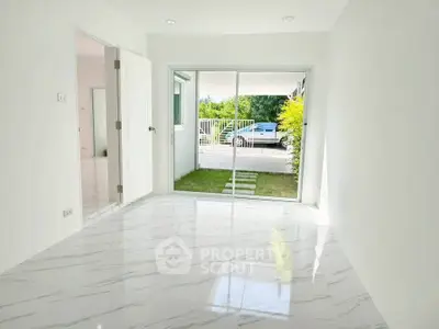 Bright empty room with marble flooring and sliding glass doors leading to a small garden area.