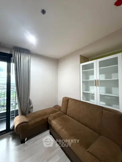 Cozy living room with brown sofa and glass cabinet, featuring a balcony view.