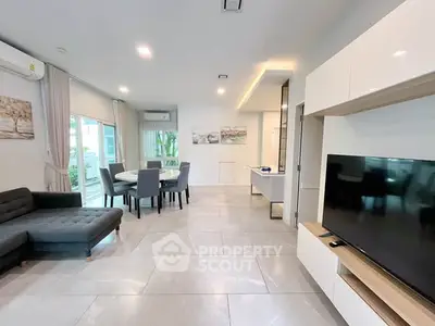 Modern living room with sleek furniture and open dining area, featuring large windows and stylish decor.